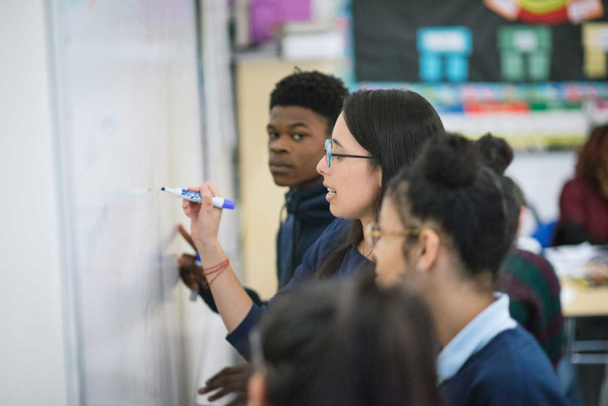 3 students collaborating on a white board in a classroom