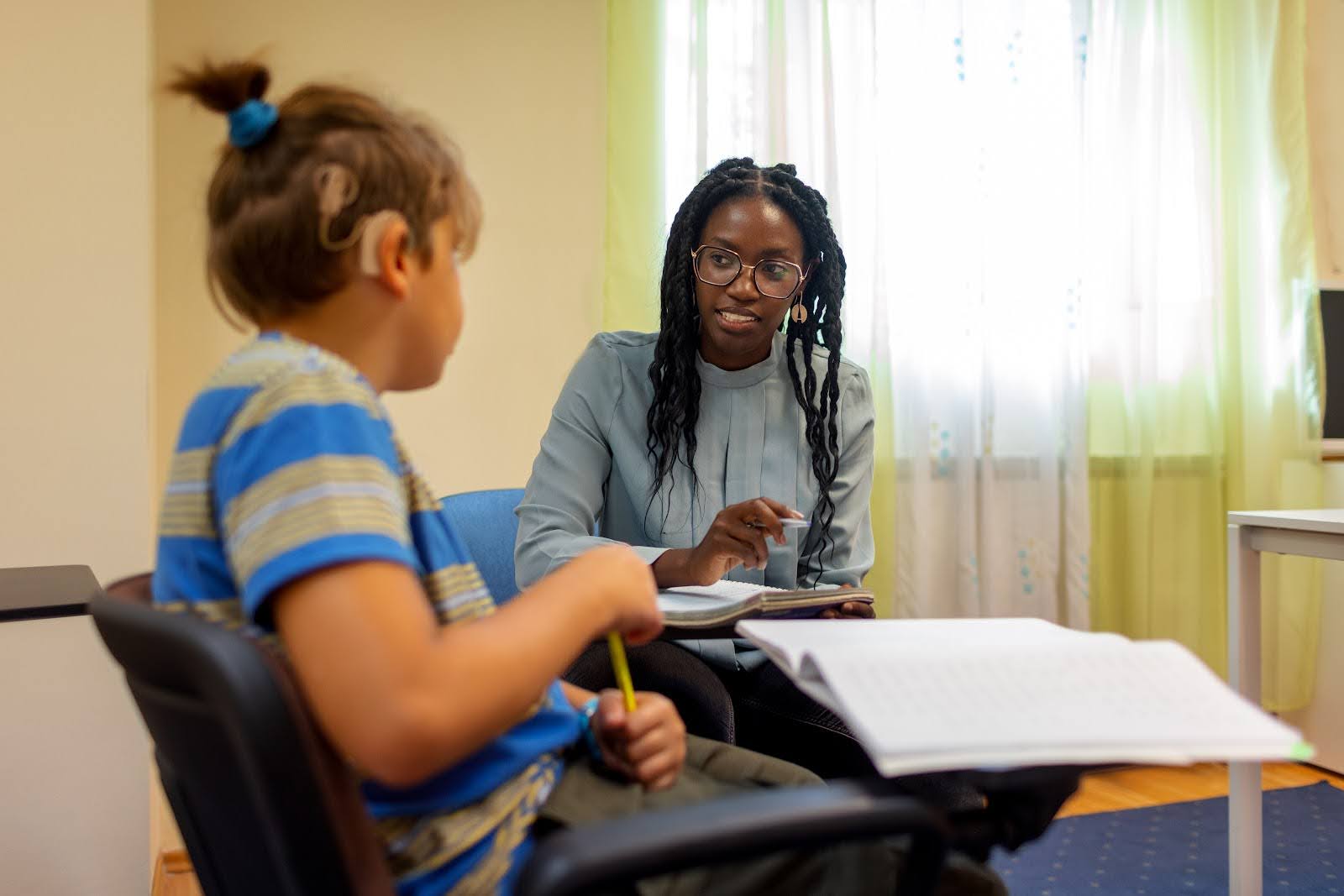 A teacher works one-on-one with a young student wearing a hearing aid.