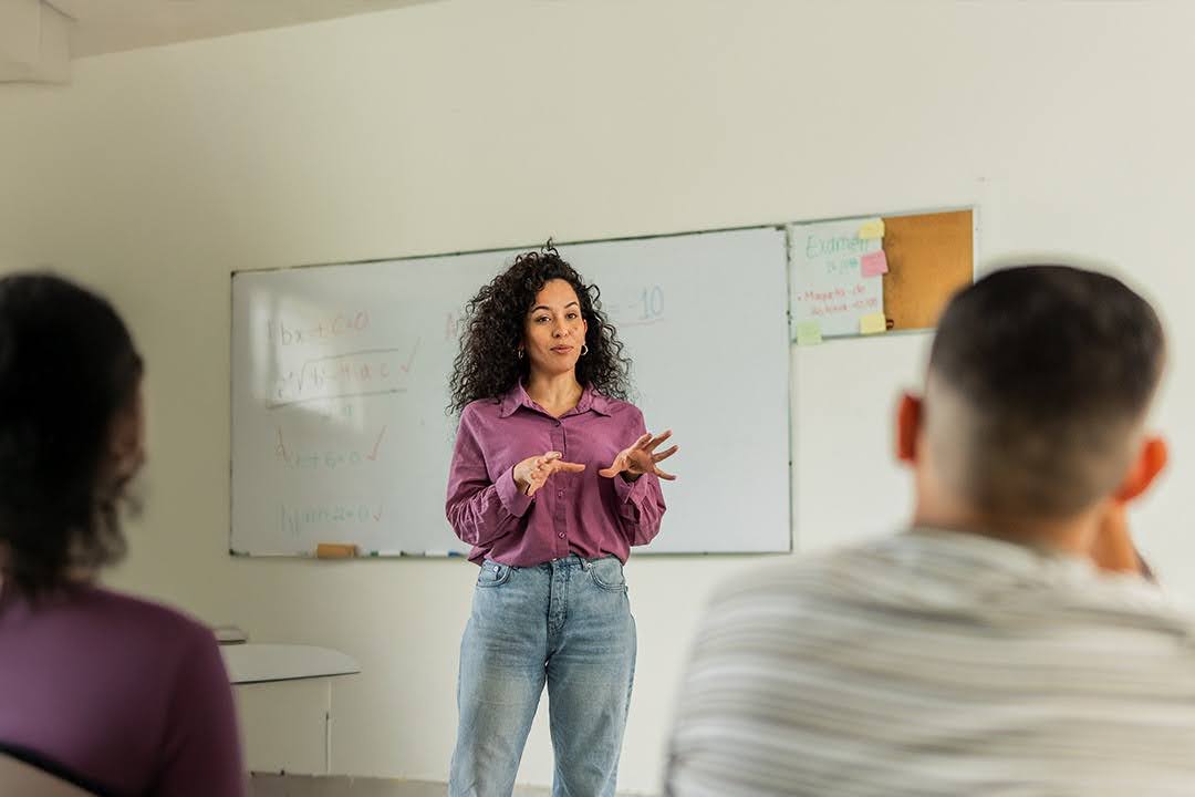 An instructor stands in front of a whiteboard, teaching math to students in a classroom.