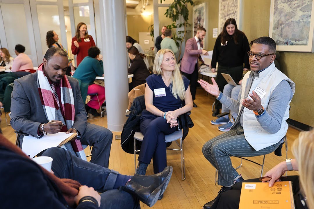 A group of teacher residents wearing nametags sit in a circle engaged in conversation.