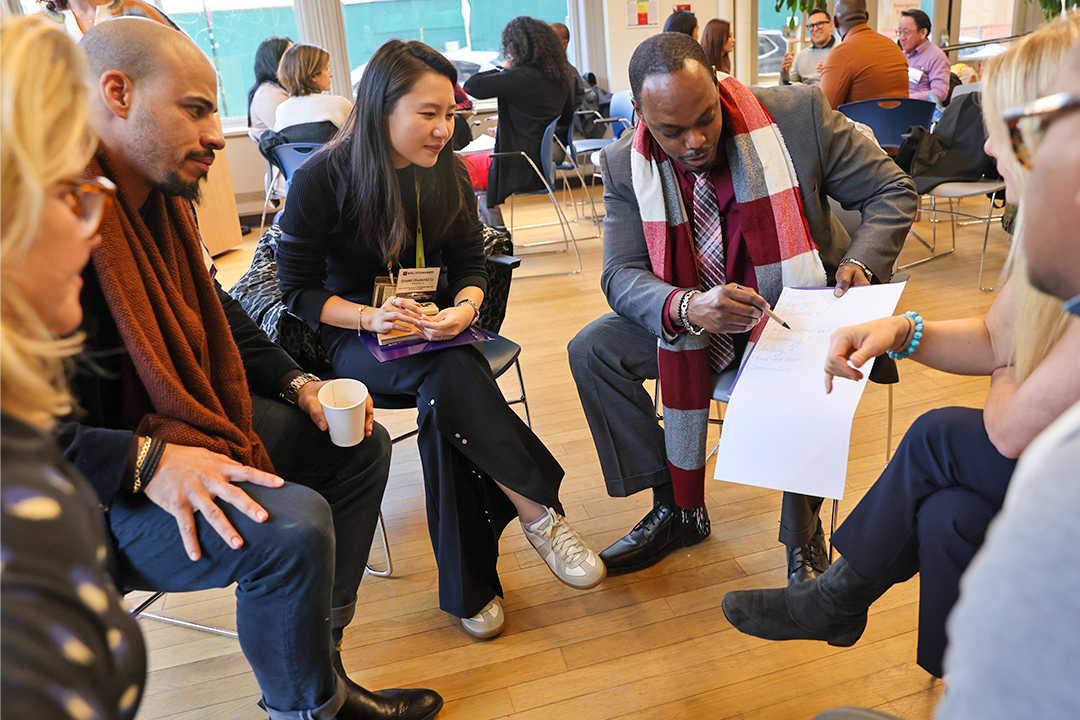 A group of professionals sit in a semi-circle and discuss a document.