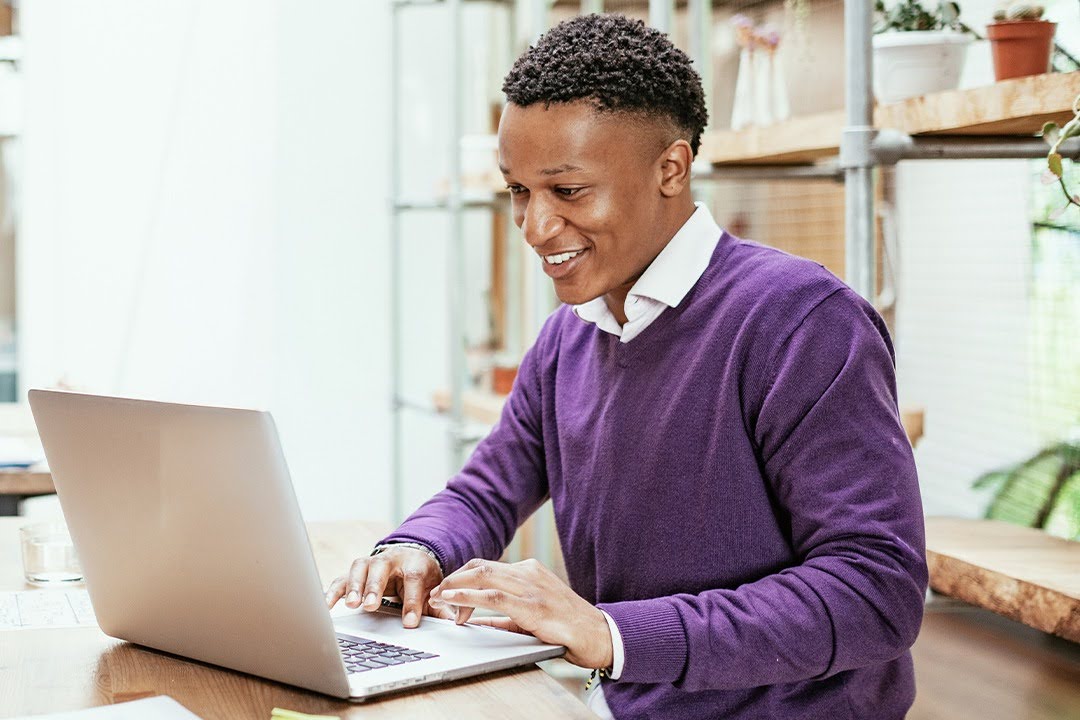 A smiling person in a bright, modern space types at a laptop.